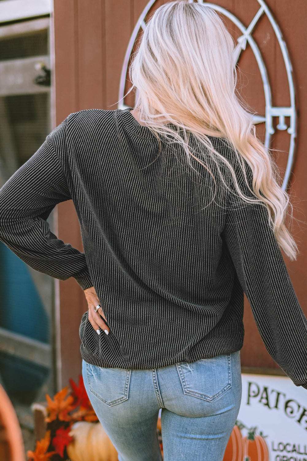 A person with long blonde hair wearing a Black NASHVILLE MUSIC CITY Corded Graphic Sweatshirt and blue jeans stands with their back facing the camera.