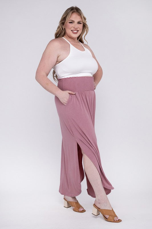 A person wearing a white top and the Plus Smocked Waist Side Slit Maxi Skirt w/ Pockets stands with crossed legs, showcasing tan heels.