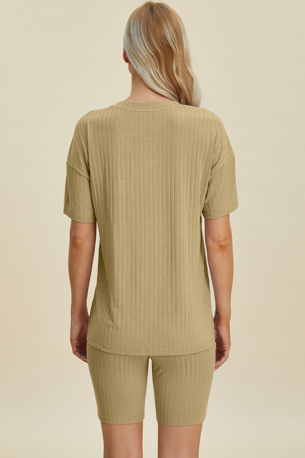 A woman with long blonde hair wearing the Basic Bae Full Size Ribbed V-Neck Short Sleeve Top and Shorts Set in rust stands against a plain background. This stylish two-piece set is made from a comfortable, stretchy fabric that is also machine washable.