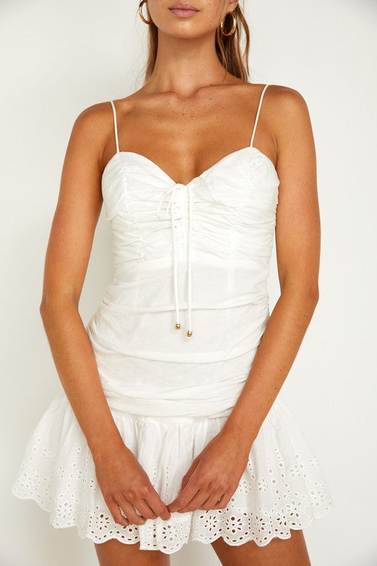 Wearing a Ruched Cami Mini Dress in a light green hue, a woman holds a wicker basket filled with dried flowers and poses elegantly against a plain white background, capturing the essence of an elegant summer wardrobe.