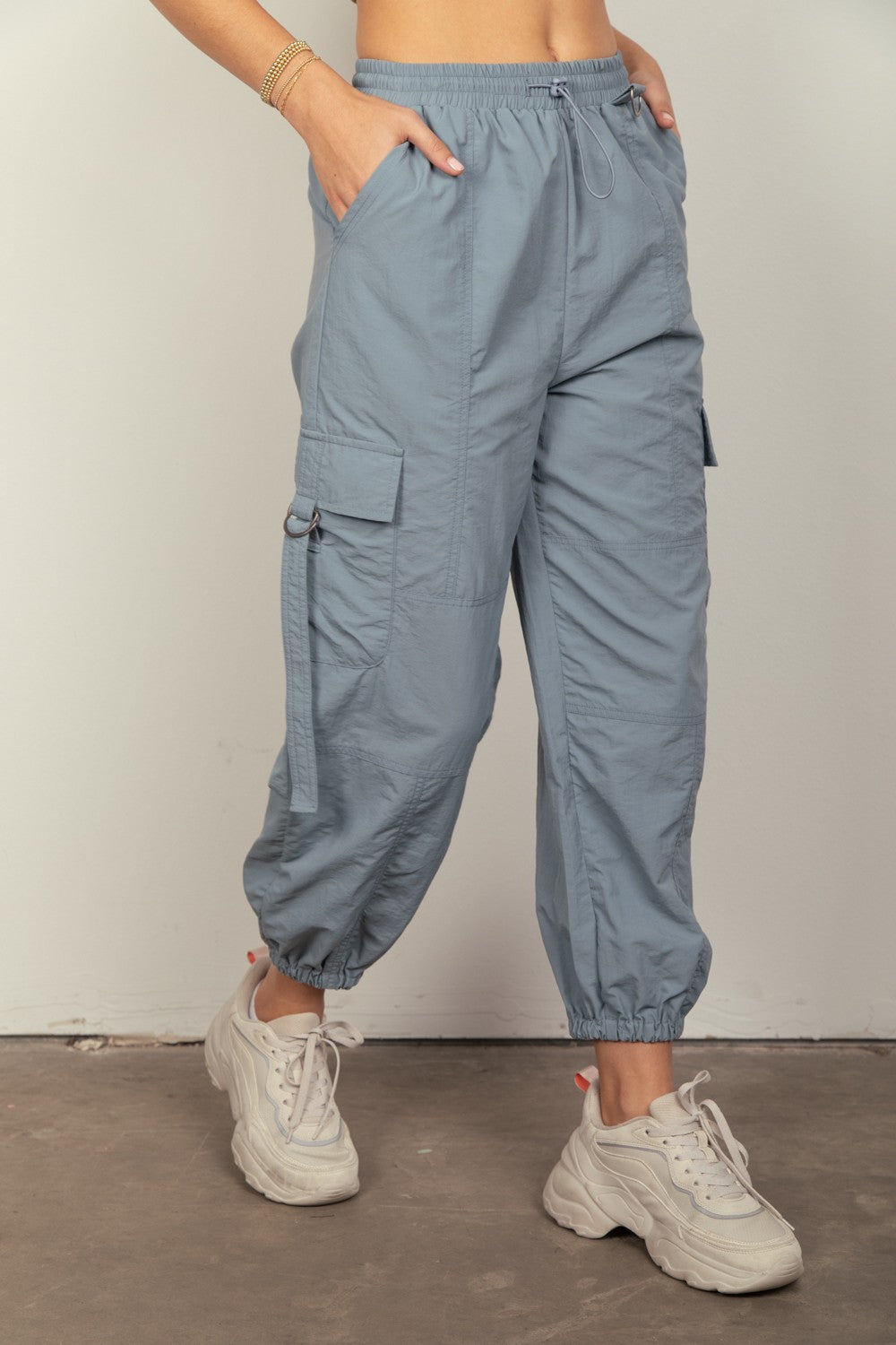 Person wearing VERY J Elastic Waist Woven Cargo Pants in light blue with hands in pockets, paired with white sneakers, standing against a plain background.