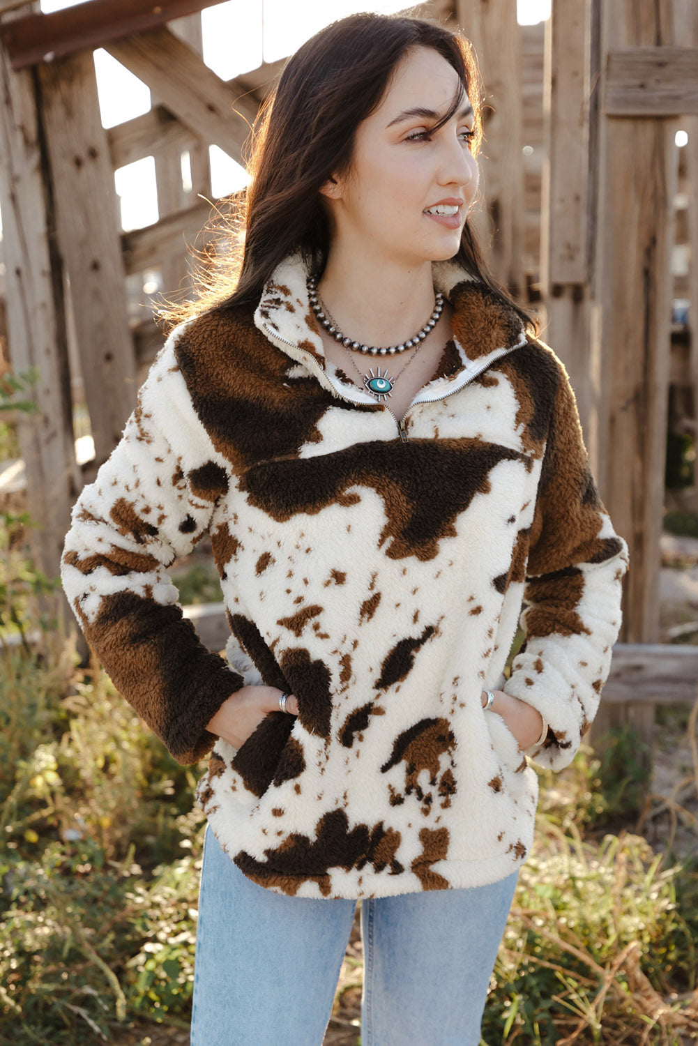 A person wearing a Zip Collar Cow Print Fleece Sweatshirt and light blue jeans stands outdoors with their back to the camera, showcasing the skin-friendly fleece material.