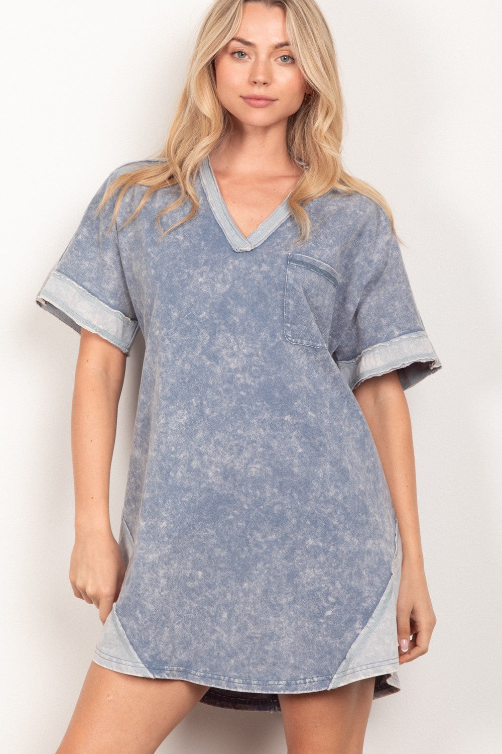 Dressed in a VERY J Short Sleeve V-Neck Tee Dress, an individual exudes a casual yet stylish vibe while posing against a simple backdrop. This adaptable piece seamlessly blends fashion and functionality, making it perfect for any occasion.