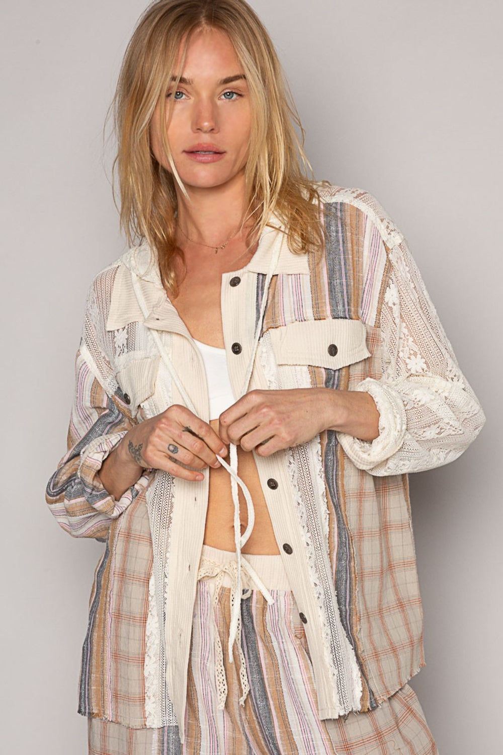 A person with long blonde hair, dressed in a mixed-patterned ensemble featuring 100% cotton lace and plaid elements, looks over their shoulder while holding the drawstring of the POL Long Sleeve Plaid Hood Shirt.