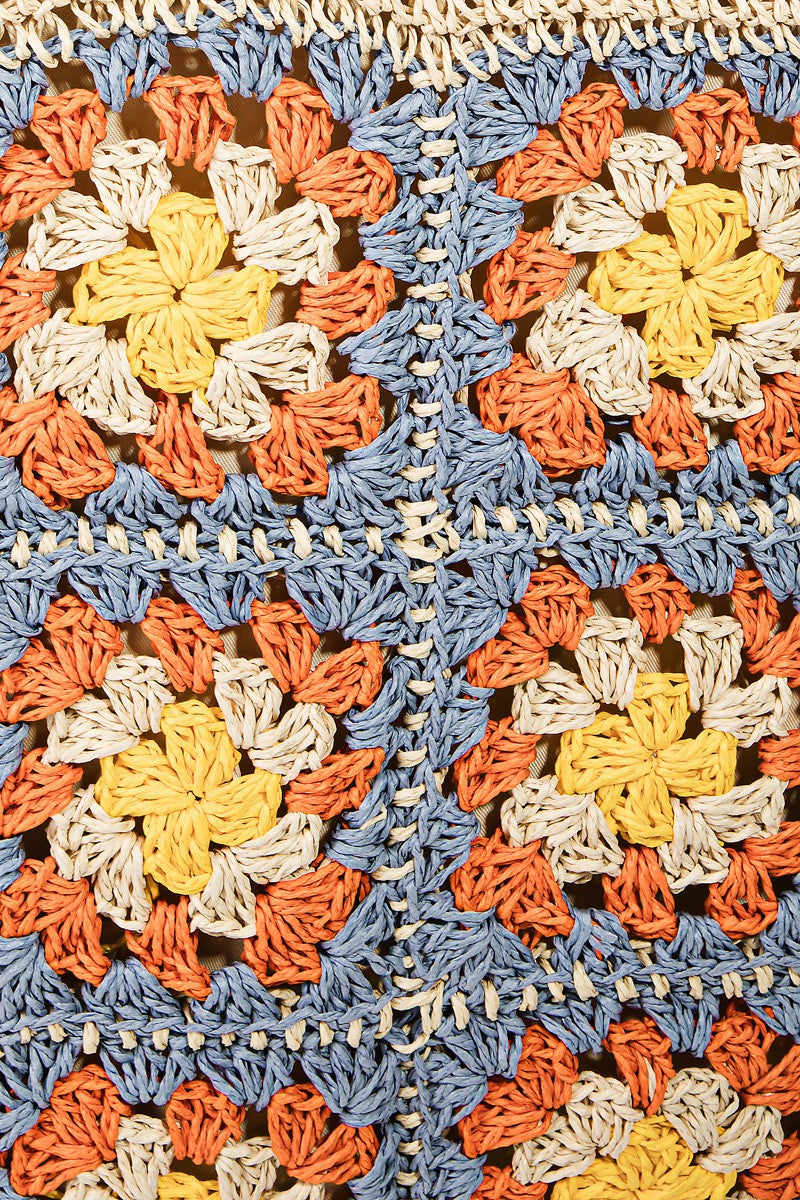 The Fame Flower Braided Tote Bag is a crocheted accessory with bohemian flair, featuring a grid of colorful flower patterns on the front. It showcases squares in orange, yellow, and blue on a natural fiber background.