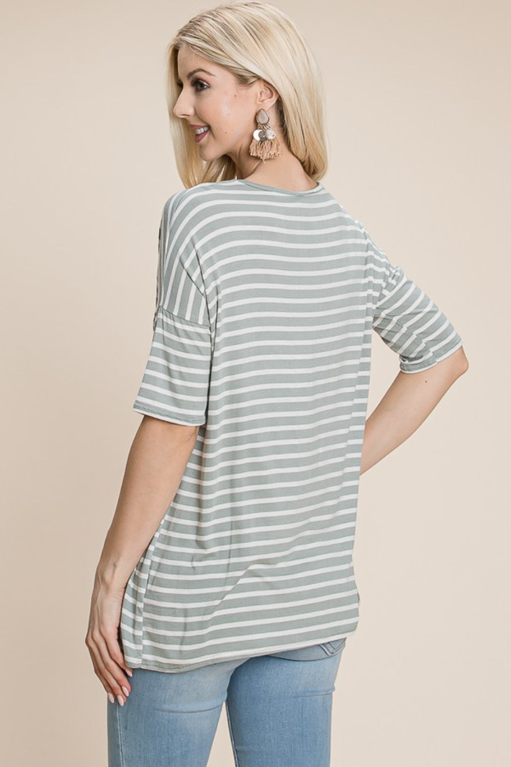 A woman with long blonde hair, dressed in a BOMBOM Striped Round Neck T-Shirt and blue jeans, exudes nautical charm while smiling and looking off to the side.