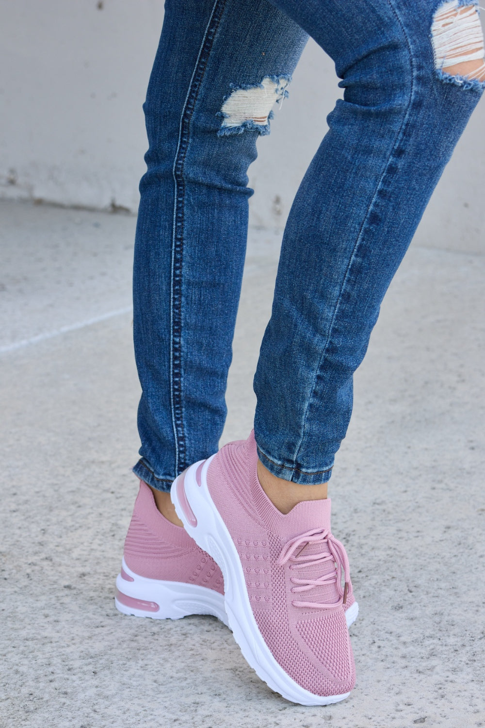 A person is wearing ripped blue jeans and Forever Link breathable mesh lace-up round toe athletic shoes, standing on a concrete surface.