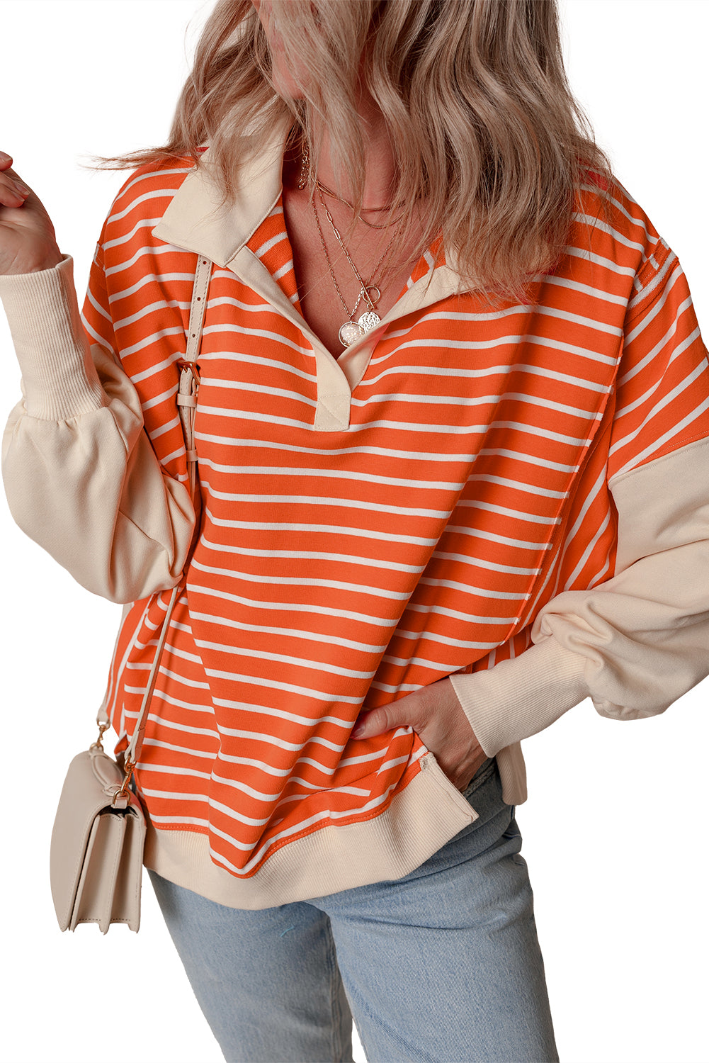 A person with wavy hair is seen from the back, wearing an Orange Stripe Color Block Loose Fit Collared Drop Shoulder Sweatshirt, light blue jeans, and carrying a small beige bag.