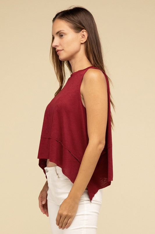 Wearing the Shark Bite Side Slit Short Sleeveless Top in maroon paired with white pants, a model is set against a beige background, exemplifying an effortlessly chic and casual wardrobe.