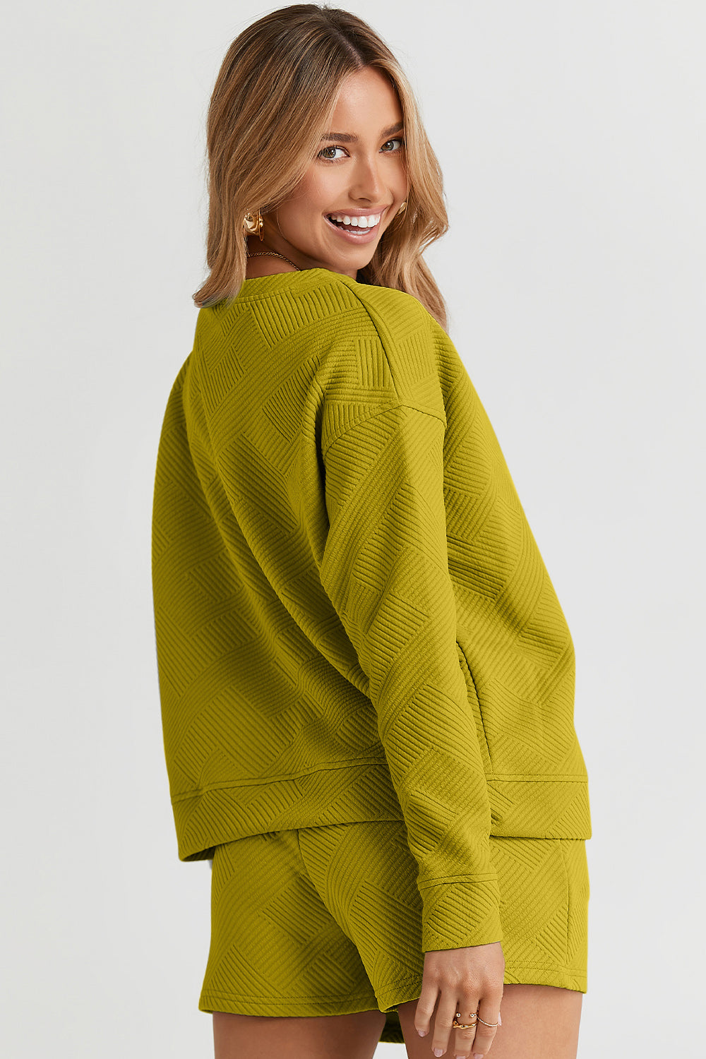 A woman decked out in the Double Take Full Size Texture Long Sleeve Top and Drawstring Shorts Set, featuring a brown textured two-piece with a long-sleeve top and matching pocketed shorts, smiles at the camera.