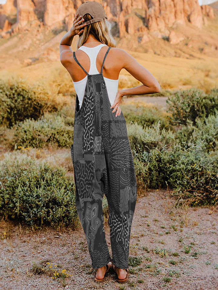 A person standing outdoors in front of rocky terrain, wearing a Full Size Printed V-Neck Sleeveless Jumpsuit and a hat.