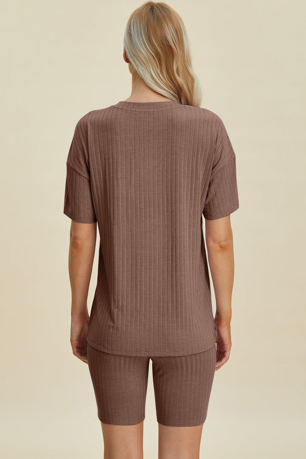 A woman with long blonde hair wearing the Basic Bae Full Size Ribbed V-Neck Short Sleeve Top and Shorts Set in rust stands against a plain background. This stylish two-piece set is made from a comfortable, stretchy fabric that is also machine washable.