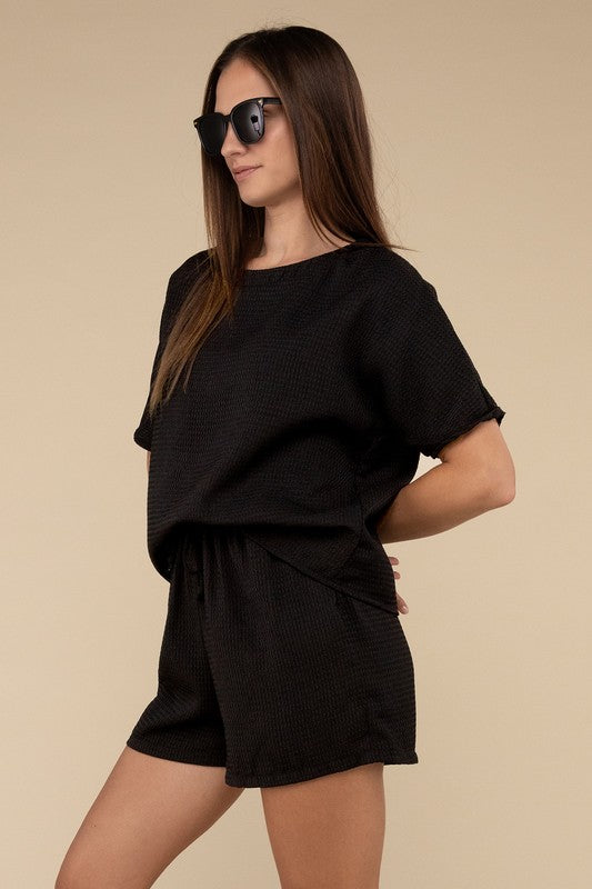 Clad in the Waffle Round Neck Top and Short Set paired with black sunglasses, a person stands against a plain beige background, highlighting the non-stretch polyester fabric.