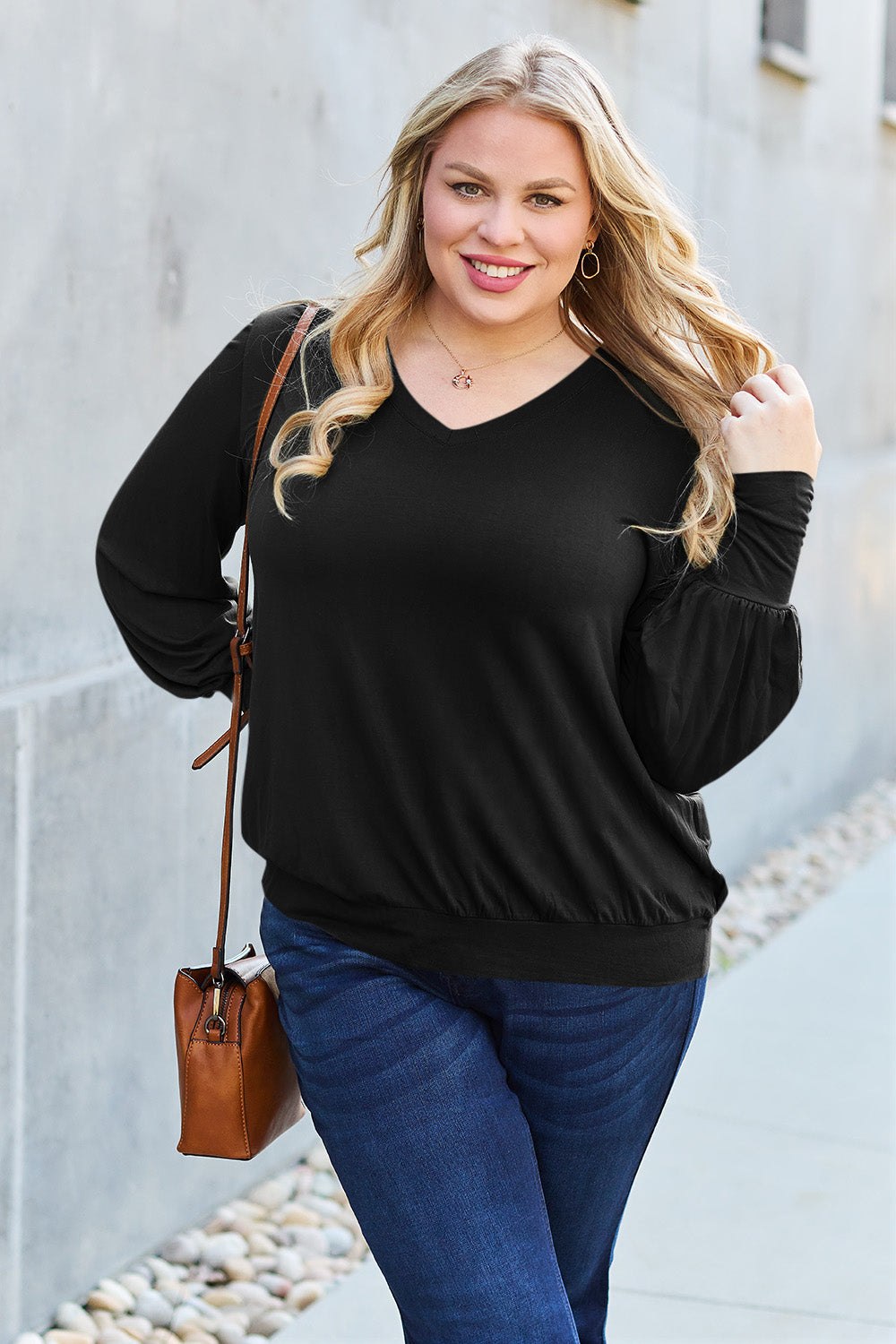 A woman with brown hair is standing against a concrete wall, wearing the Basic Bae Full Size V-Neck Lantern Sleeve Top in teal and blue basic-style jeans, smiling.