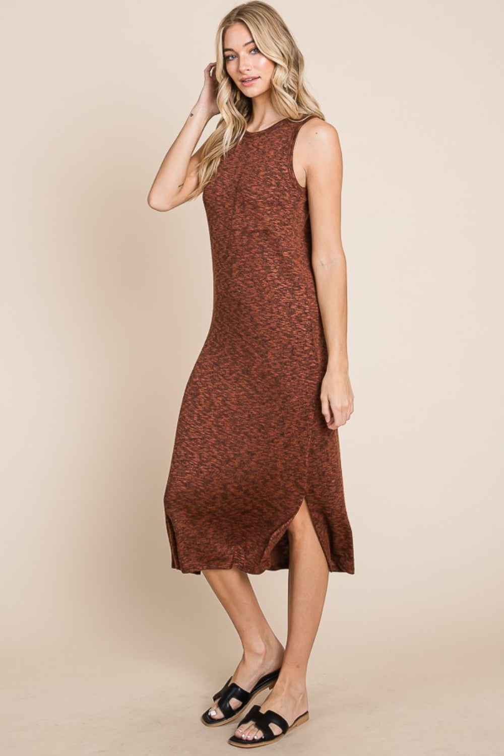 A woman with long blonde hair stands against a beige background, wearing the versatile and stylish BOMBOM Slit Round Neck Sleeveless Midi Dress in rust color, featuring a slit round neck and side slit, paired with black sandals.