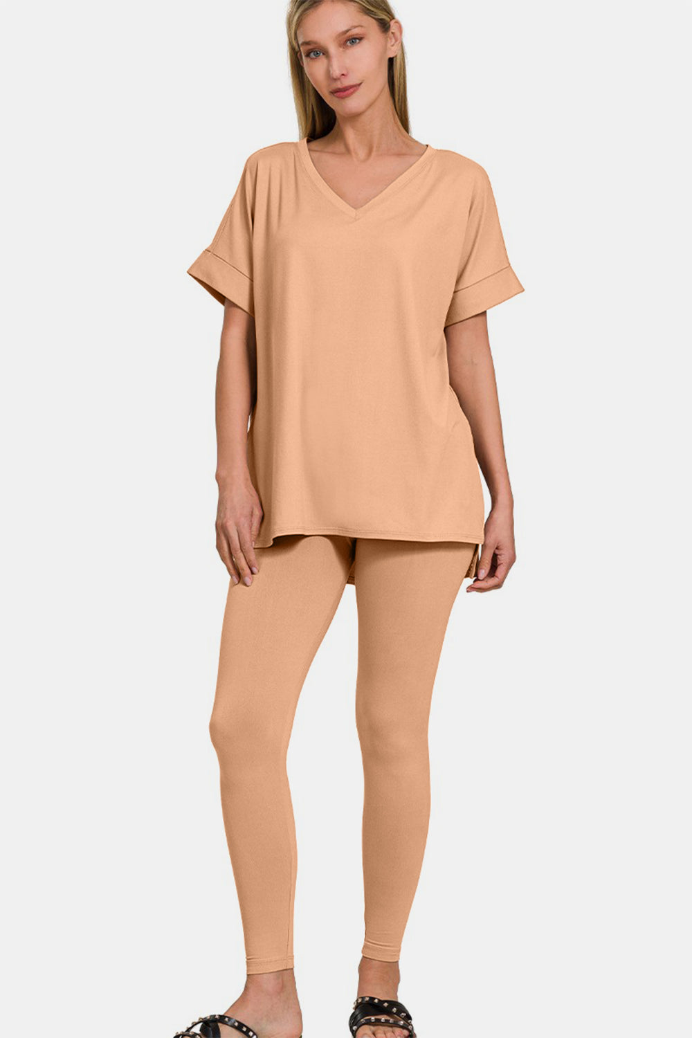 Against a simple backdrop, someone wears the Zenana Full Size V-Neck Rolled Short Sleeve T-Shirt and Leggings Lounge Set, seamlessly blending comfort and style with its chic beige ensemble.