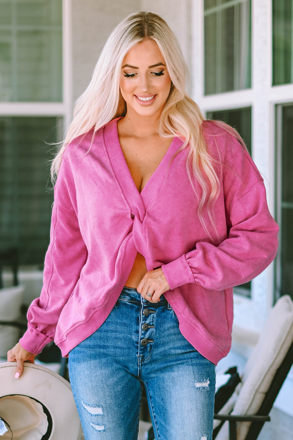 A woman stands with her back to the camera, wearing a long-sleeved Rose Exposed Seam Twist Open Back Oversized Sweatshirt and light blue jeans, showcasing a relaxed fit.