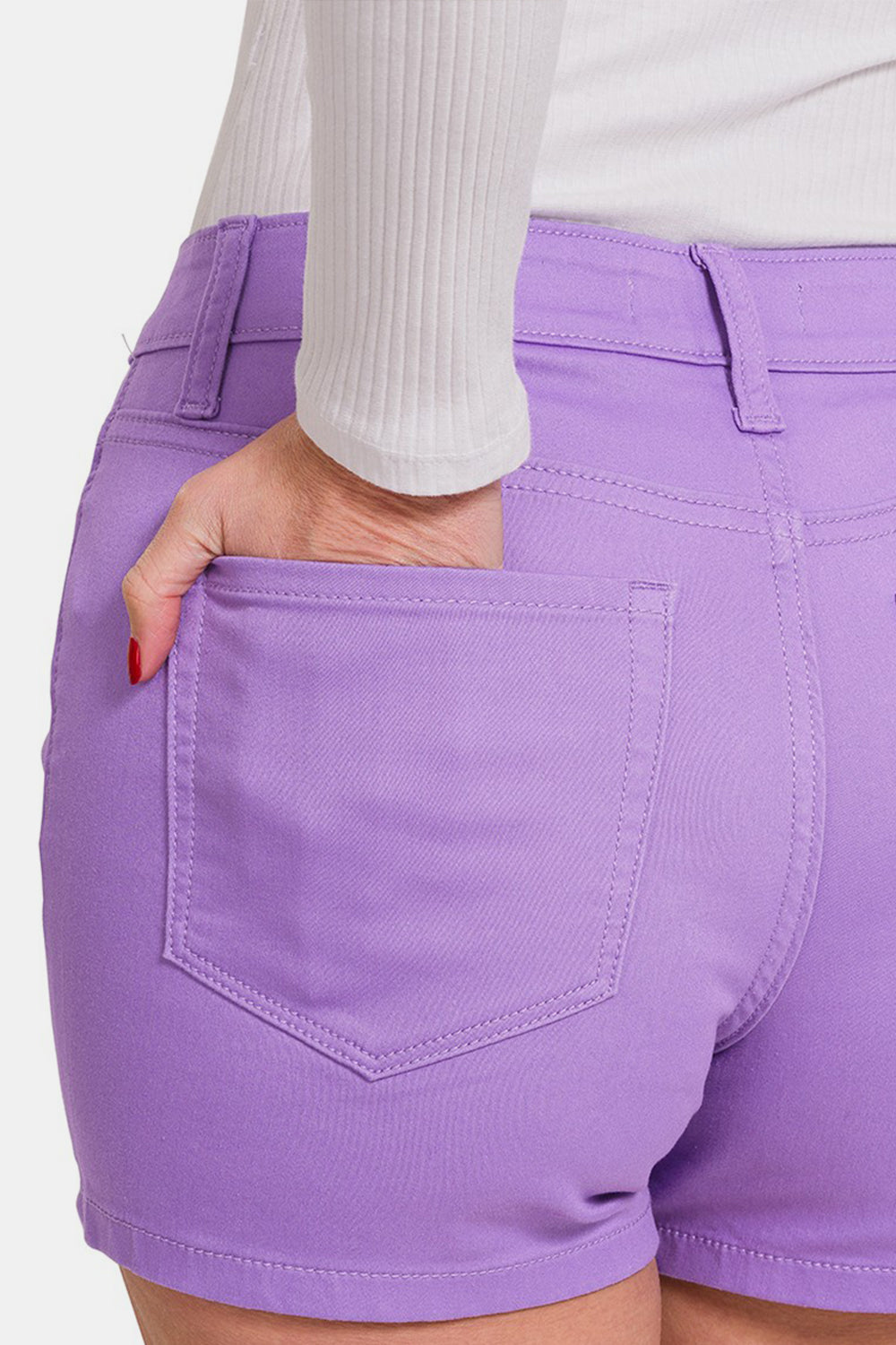 A person wearing Zenana High Waist Denim Shorts in a lavender color paired with a white long-sleeved top. The durable shorts feature belt loops, front pockets, and are secured with a button and zipper.