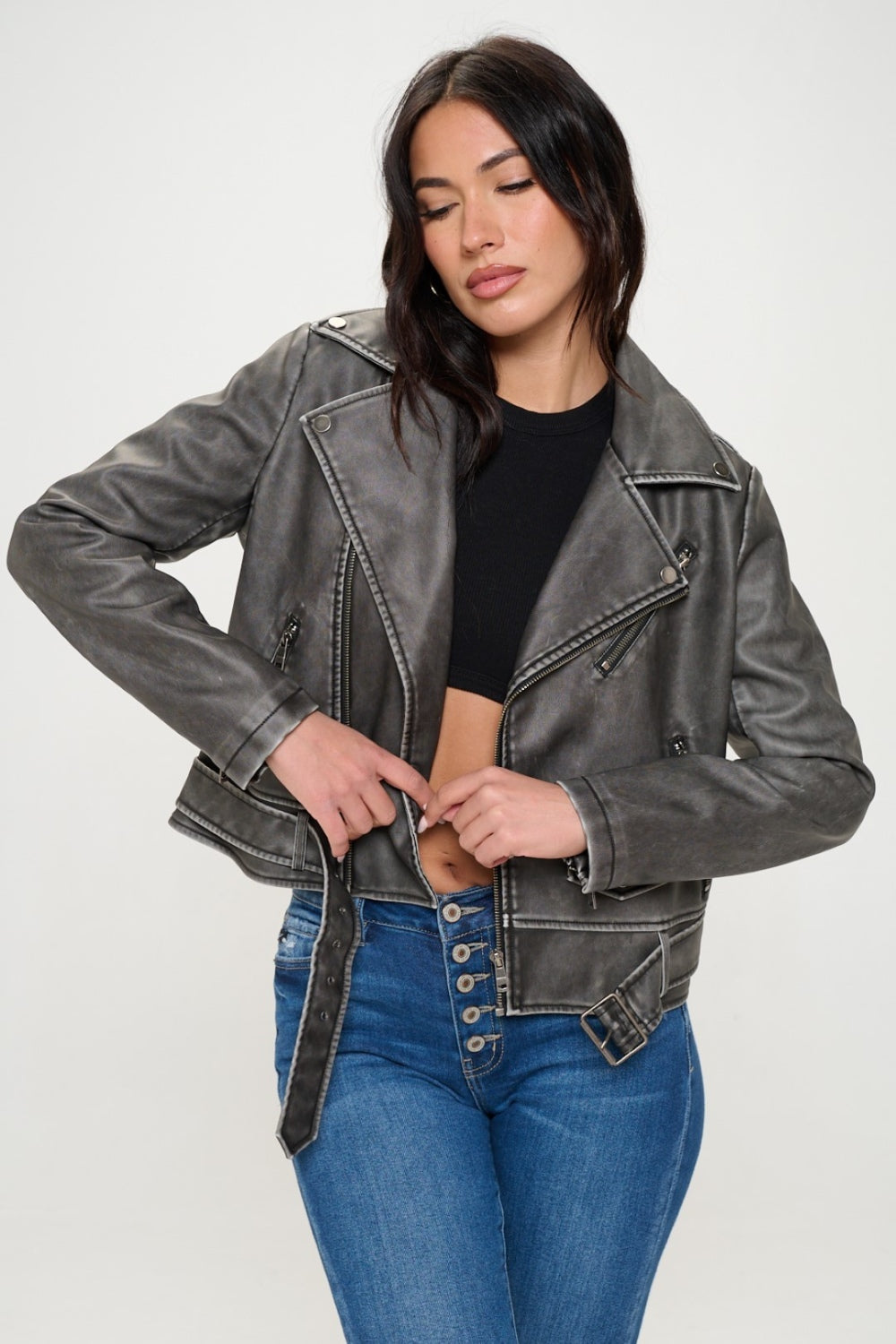 A person wearing a Coalition LA Zip Up Biker Jacket with Belt featuring a notched lapel, paired with blue jeans, stands against a plain background.