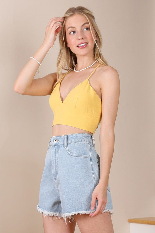 A person wearing an SL yellow crop tank top and denim shorts stands against a neutral background.