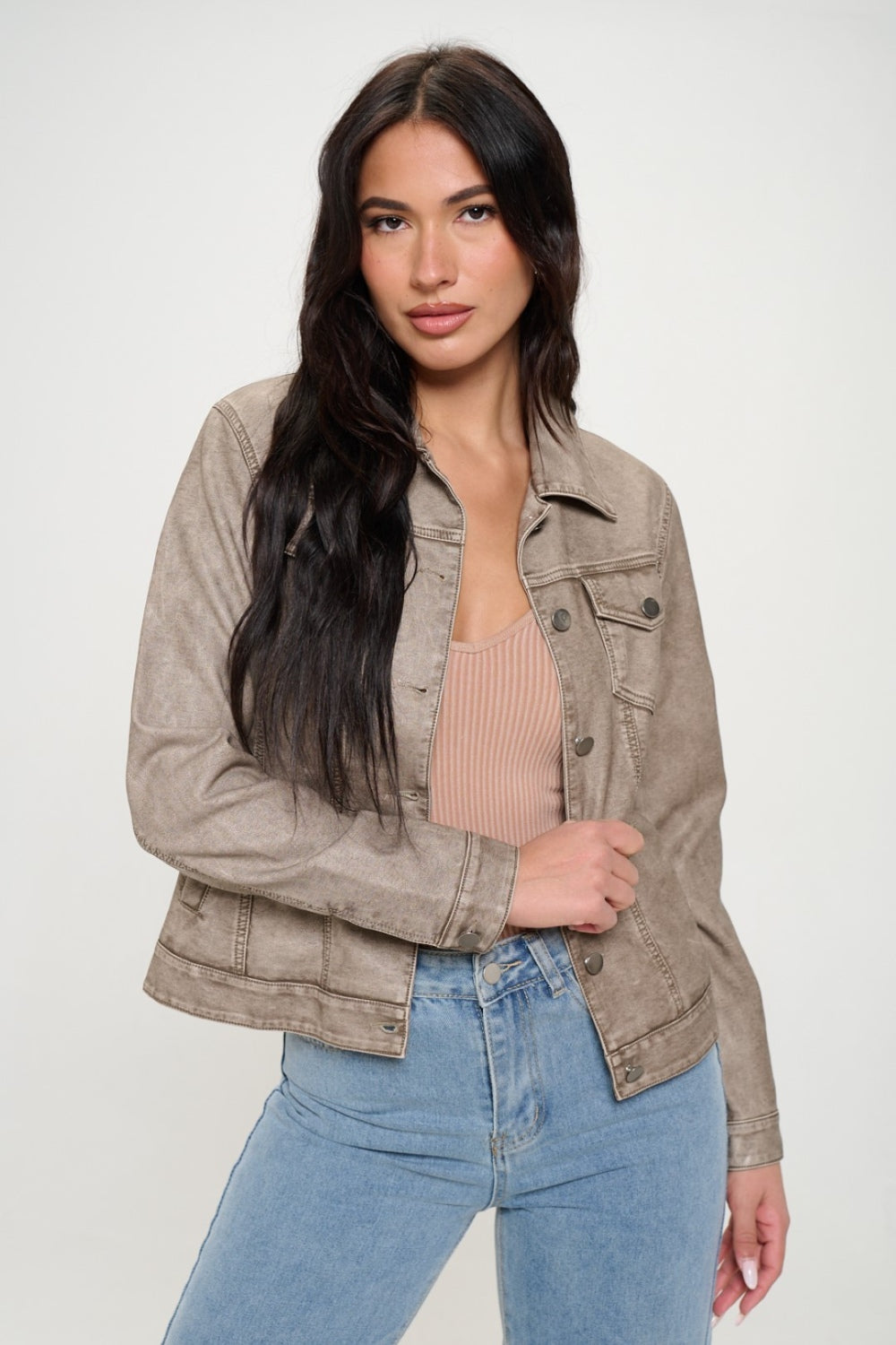 A woman with long dark hair wears a Coalition LA Button Down Cargo Vegan Leather Shacket in light beige over a ribbed top and blue jeans, standing against a light background.