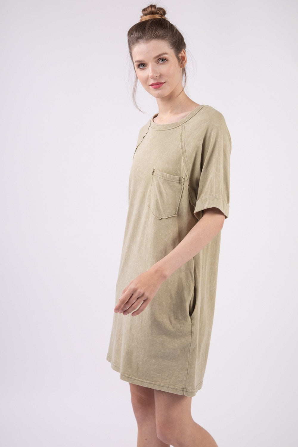 A woman in a VERY J Washed Round Neck Mini Tee Dress poses gracefully against a plain background. Her casual ensemble features an oversized beige tee dress complete with a pocket, radiating effortless style and comfort.