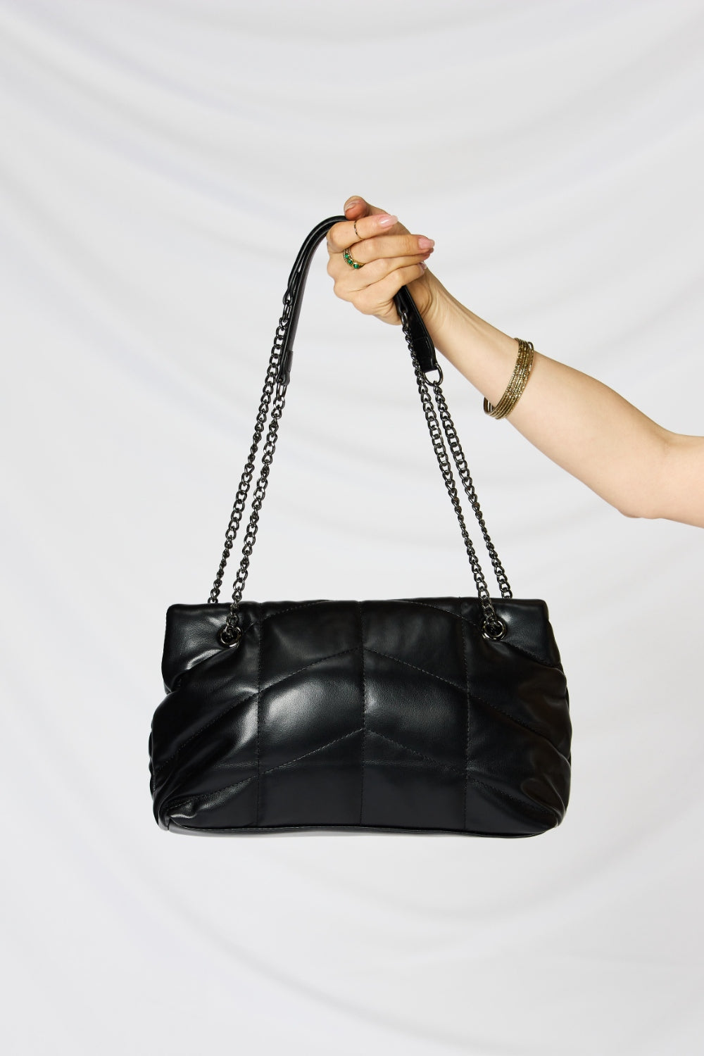 A person holding a stylish SHOMICO PU Leather Chain Handbag over their shoulder against a white background. They are dressed in a beige outfit and looking at the camera, embodying sustainable fashion.