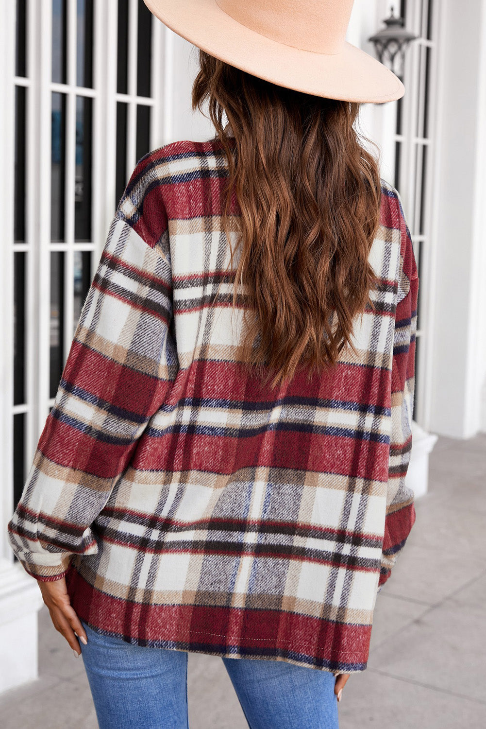 A person wearing a Brown Plaid Button Up Long Sleeve Flannel Shacket layered over a white top with ripped jeans and holding a brown handbag stands against a textured gray wall.