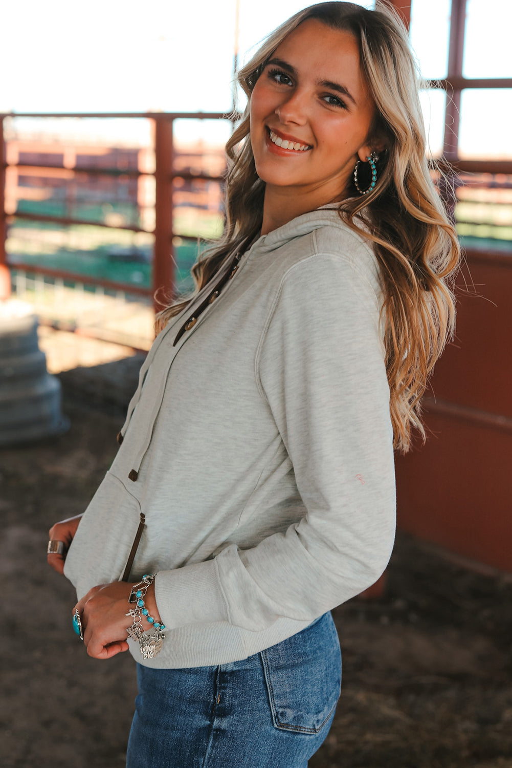 A person with long blonde hair is seen from the back wearing a Beige Drawstring Kangaroo Pocket Henley Hoodie and jeans.