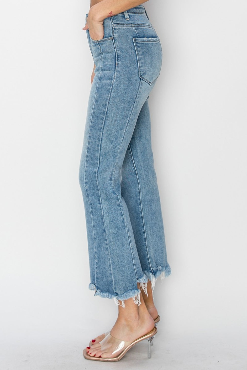 Person wearing RISEN Full Size High Rise Frayed Hem Flare Jeans with clear high-heeled shoes, standing against a plain white background.