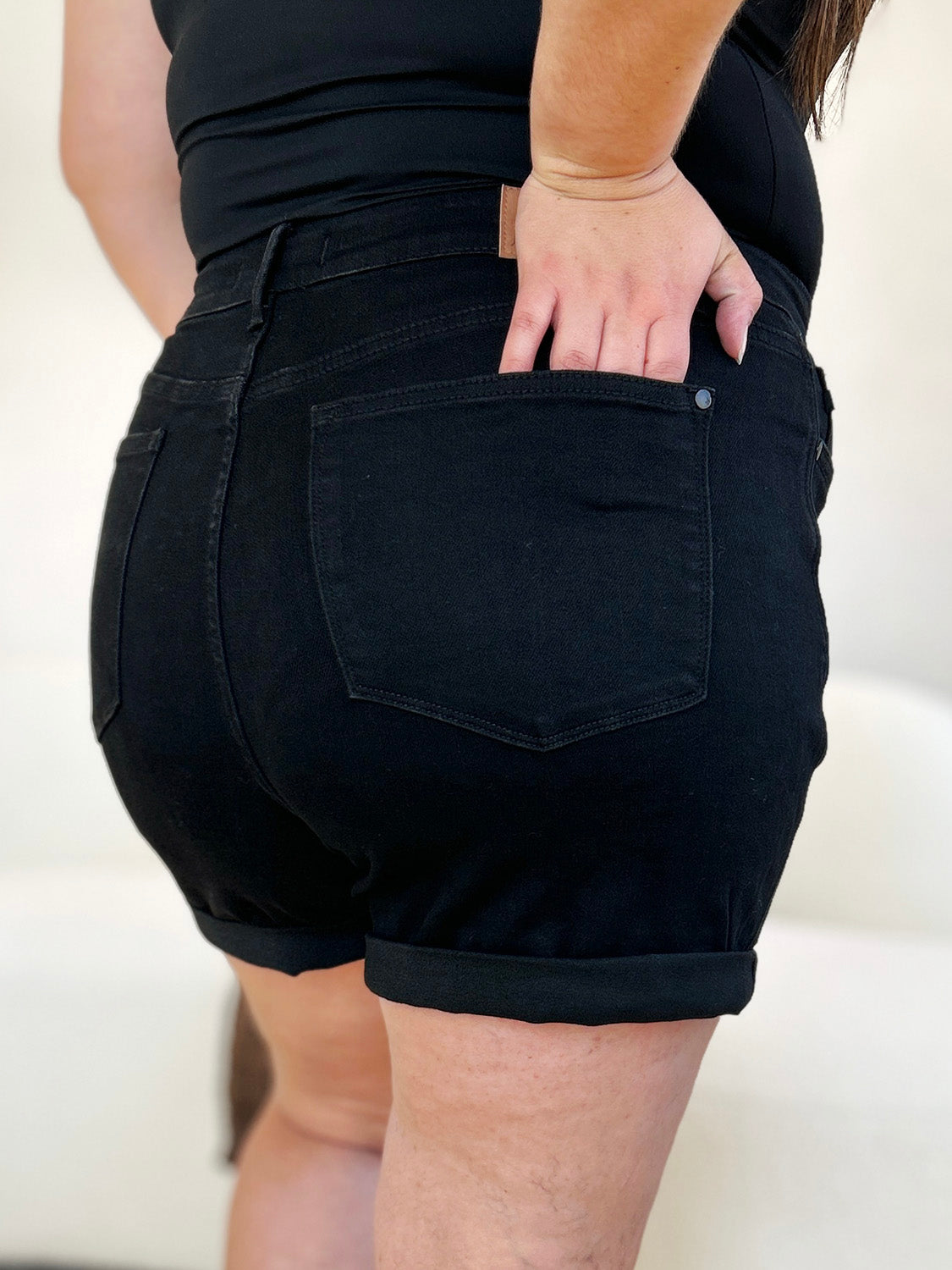 Person wearing a white top and Judy Blue Full Size High Waist Tummy Control Cuffed Denim Shorts, one hand in pocket.