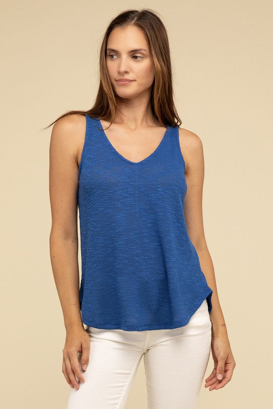 A woman in a stylish and adaptable V Neck Sleeveless Cami Top paired with jeans stands against a beige background. She has long brown hair and maintains a neutral expression.