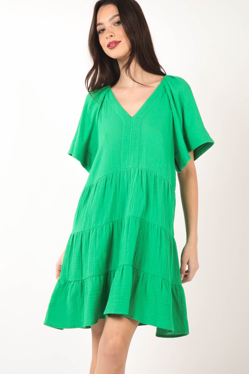 A woman poses against a white background, elegantly showcasing the flattering silhouette of the VERY J Texture V-Neck Ruffled Tiered Dress.