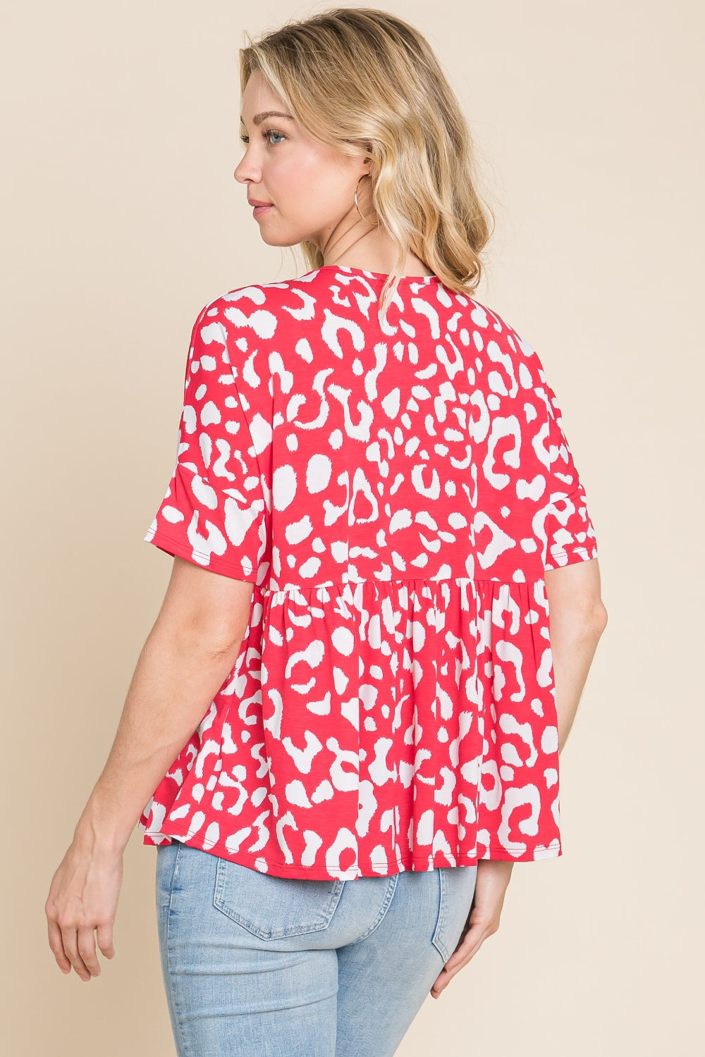 A person in a red and white BOMBOM Leopard Peplum Babydoll Blouse and blue jeans stands against a beige background.