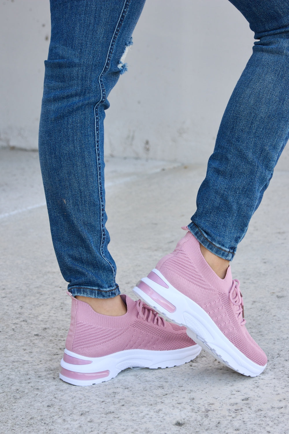 A person is wearing ripped blue jeans and Forever Link breathable mesh lace-up round toe athletic shoes, standing on a concrete surface.