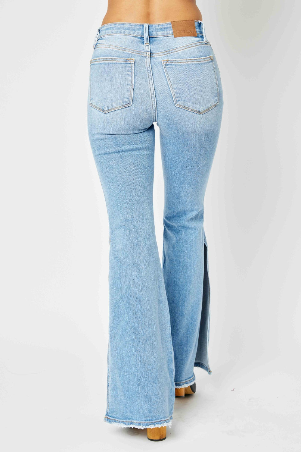 A person is wearing Judy Blue Full Size Mid Rise Raw Hem Slit Flare Jeans with a flattering silhouette and black open-toe shoes.