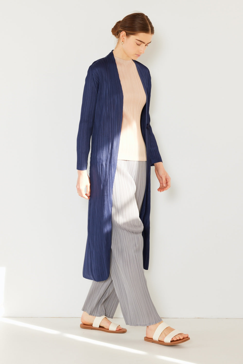 A person wears the Marina West Swim Pleated Long Sleeve Cardigan over a matching top and gray wide-leg pants, standing against a plain light background. This versatile layering piece, with its chic pleated long sleeves, adds an elegant touch to the ensemble.