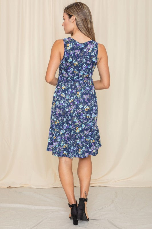 A woman in a Sleeveless Botanical Floral Tiered Dress and black sandals stands elegantly in front of a pink curtain.