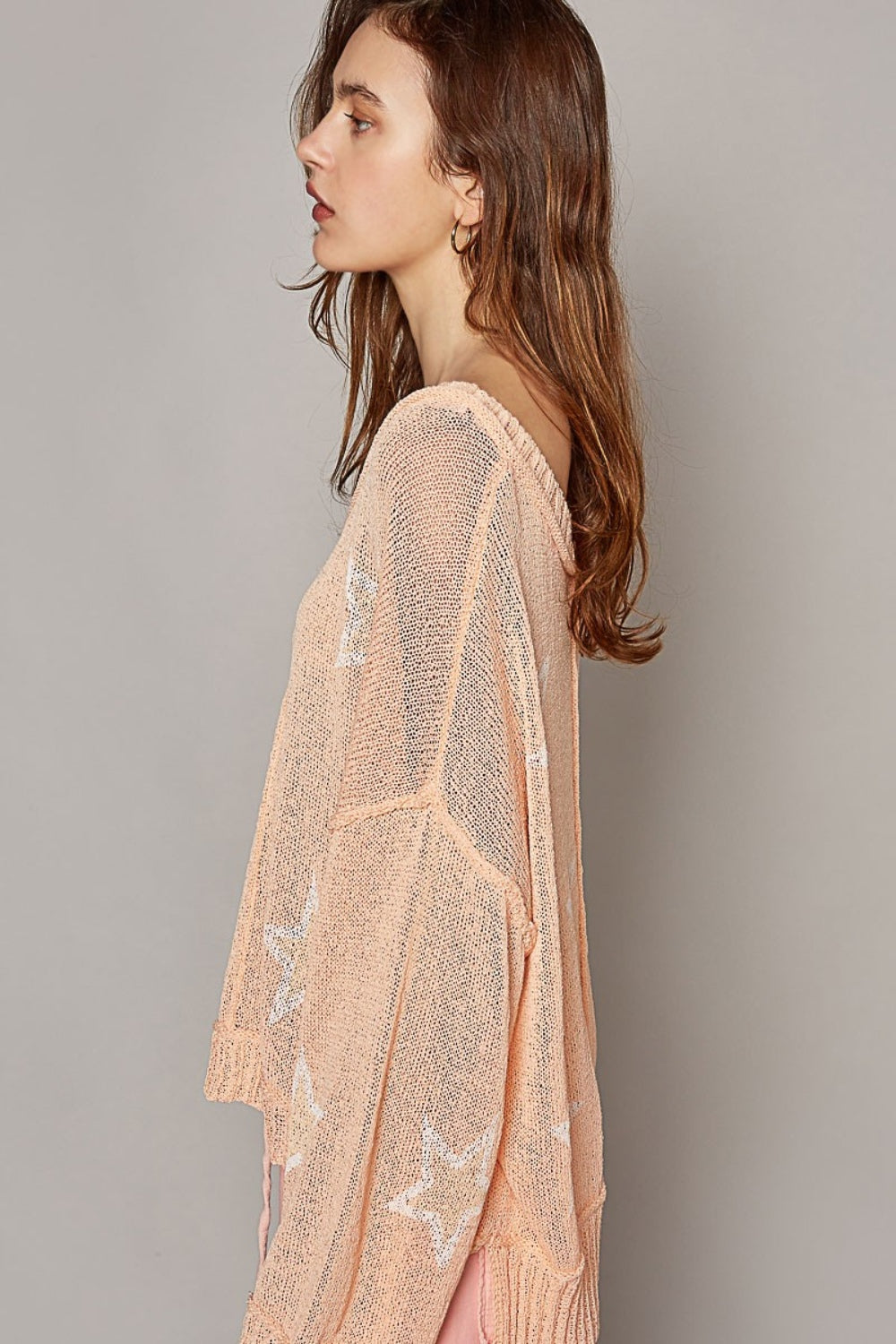 A woman with long hair is sitting down, wearing a fashionable POL V-Neck Long Sleeve Star Print Knit Top in a peach, loose-knit design. The top is paired perfectly with matching peach pants. She looks directly at the camera with a neutral expression.