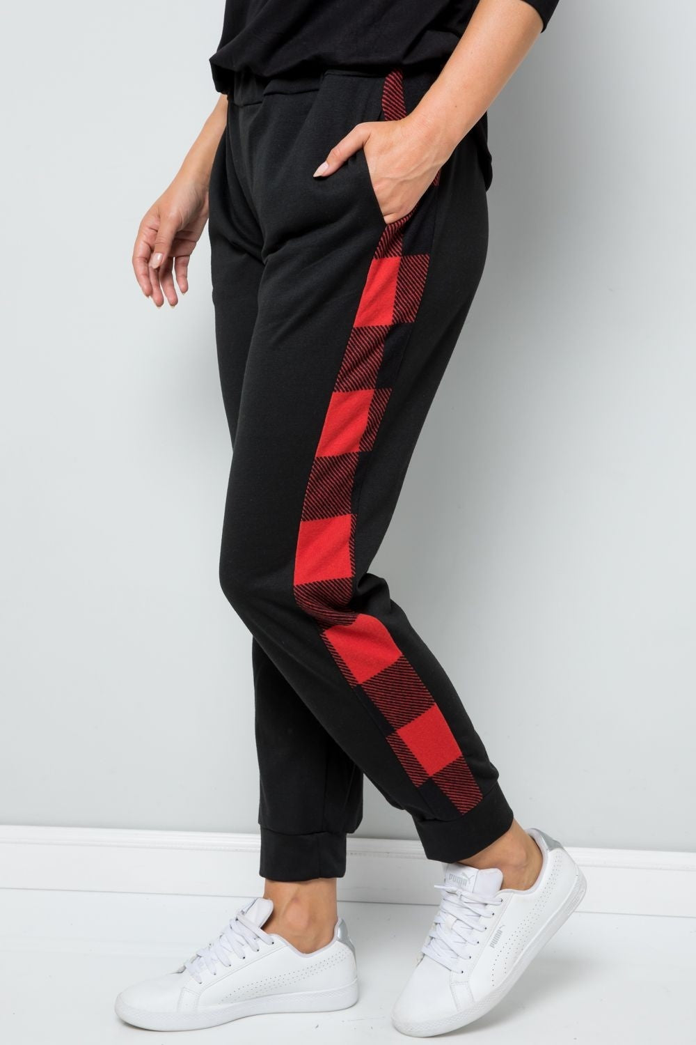 A person wearing fashionable Celeste Design Full Size Plaid Side Print Sweatpants and white sneakers stands against a gray wall.