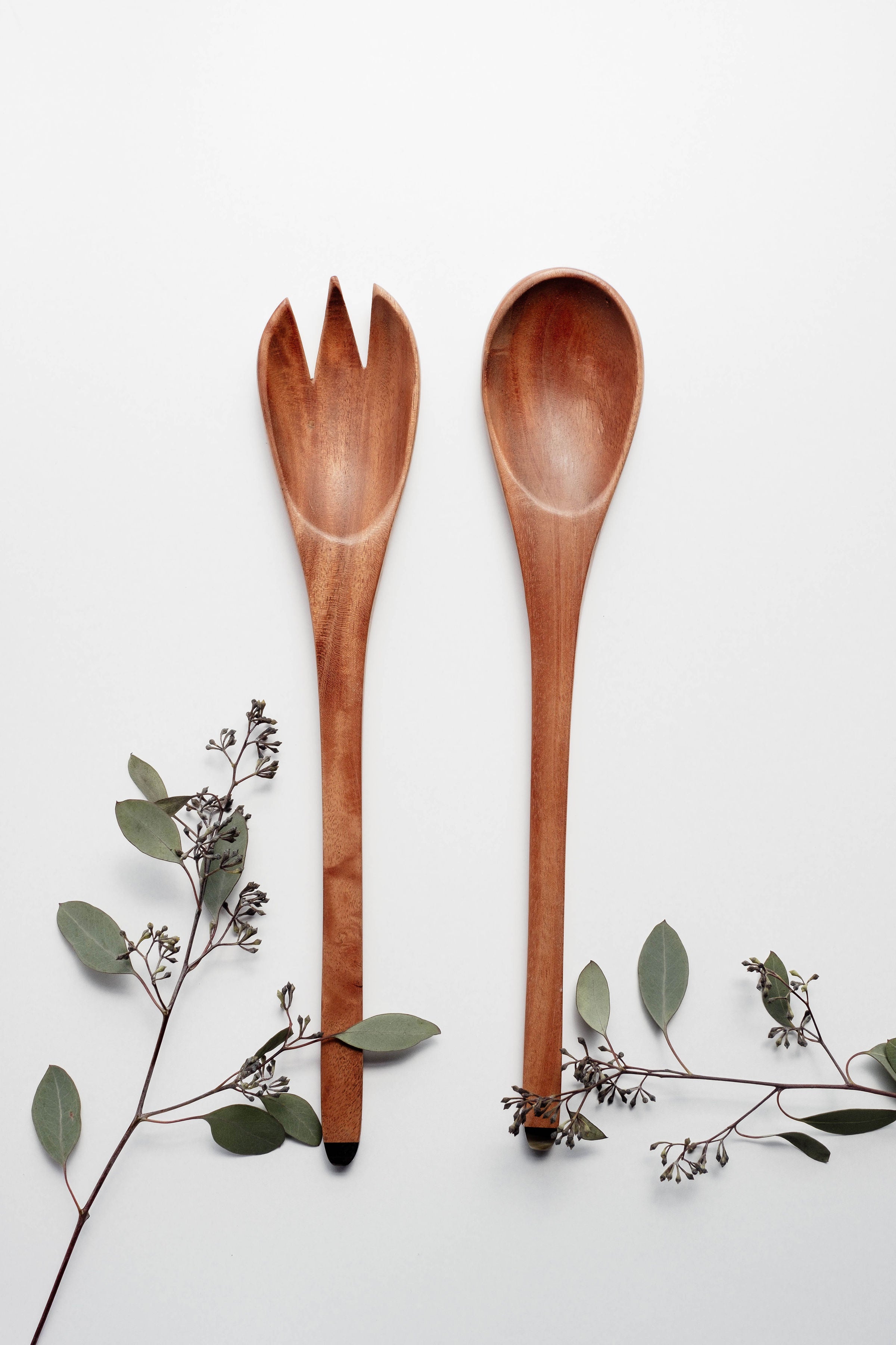 The Suzy Salad Servers, with horn-tipped handles, are elegantly displayed against a white background, complemented by sprigs of eucalyptus.