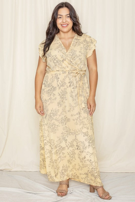 A woman wearing a Floral Surplice Sash Sundress, which is light yellow and unlined, stands smiling against a cream-colored background.