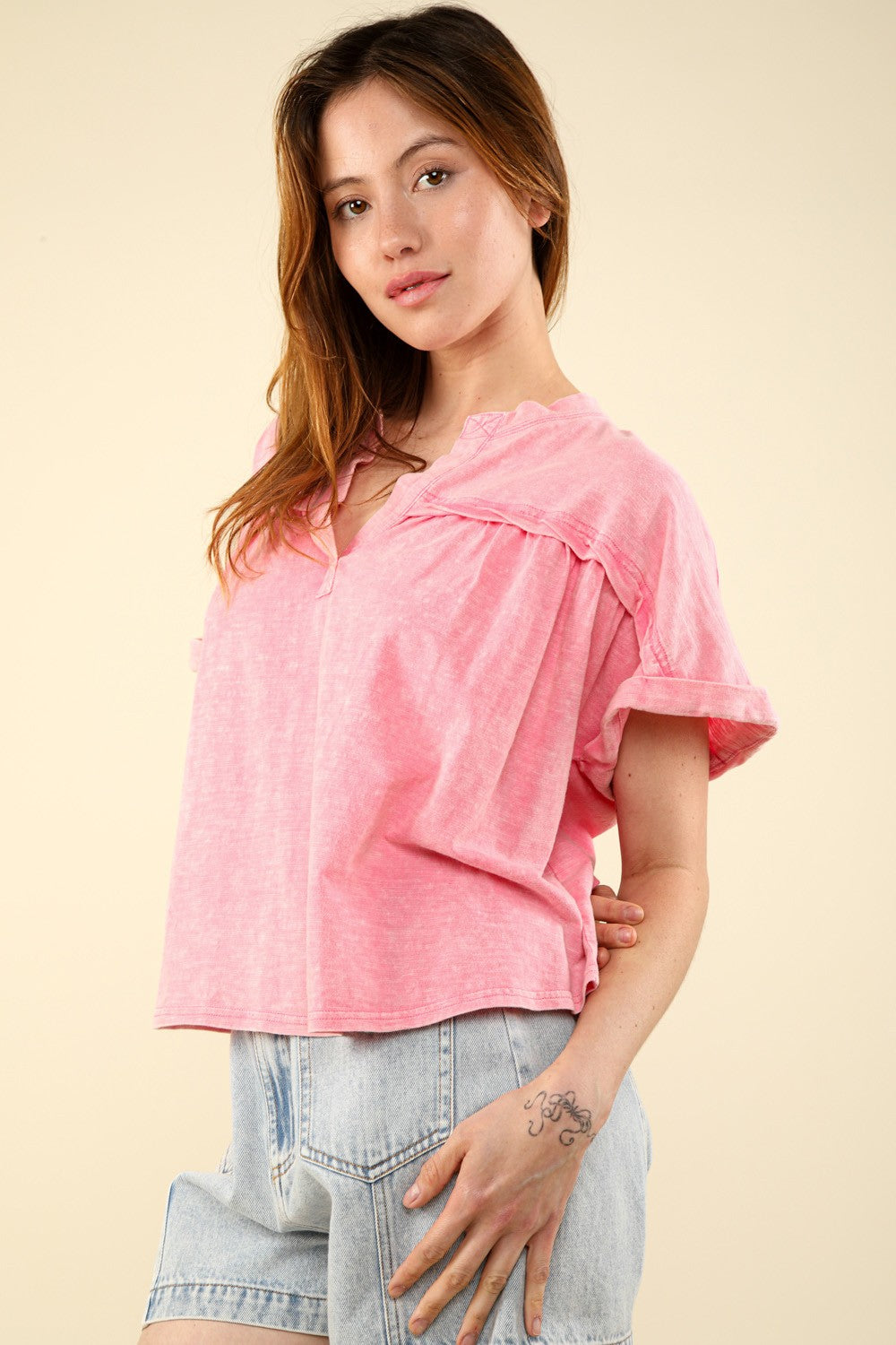 A woman in a casual fit with a VERY J Notched Short Sleeve Washed T-Shirt and light denim shorts stands against a plain background, capturing the essence of everyday wear.