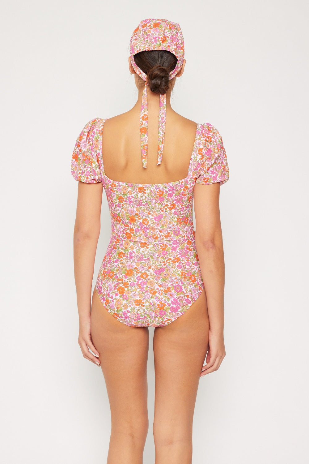 A woman poses in the Marina West Swim Floral Puff Sleeve One-Piece swimsuit, which features removable pads and comes with a matching headband, set against a plain background.