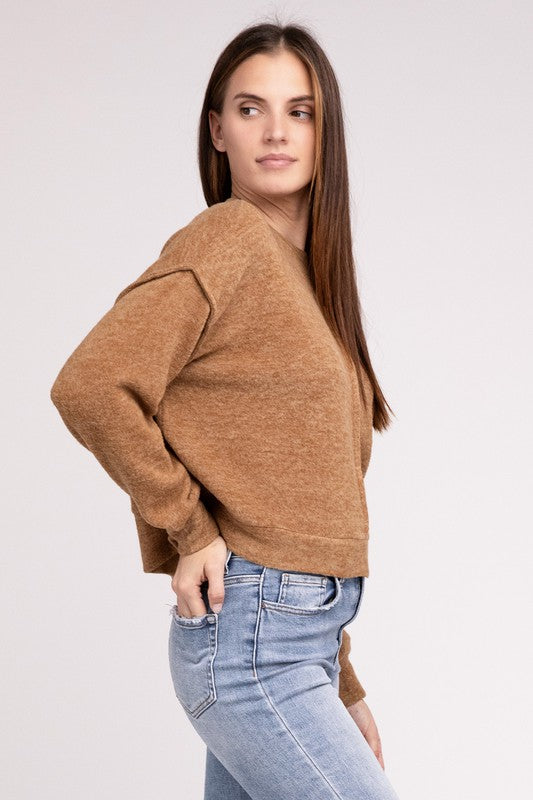 A woman in a pink Brushed Melange Hacci Hi-Low Hem Sweater and blue jeans standing with her hands clasped, against a gray background.