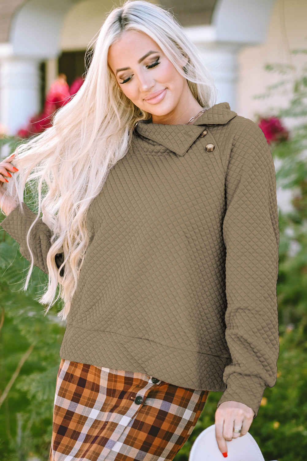 A person wearing an Apricot Quilted Buttoned Neckline Stand Neck Pullover Sweatshirt with light blue jeans holds a beige clutch while walking away on a city sidewalk.