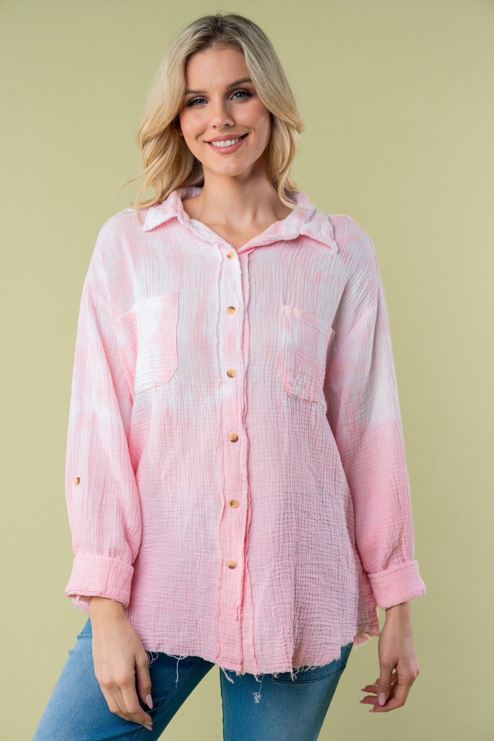 A person wearing the White Birch Full Size Long Sleeve Tie Dye Shirt with rolled-up sleeves stands against a plain background, holding a strand of their hair with one hand.