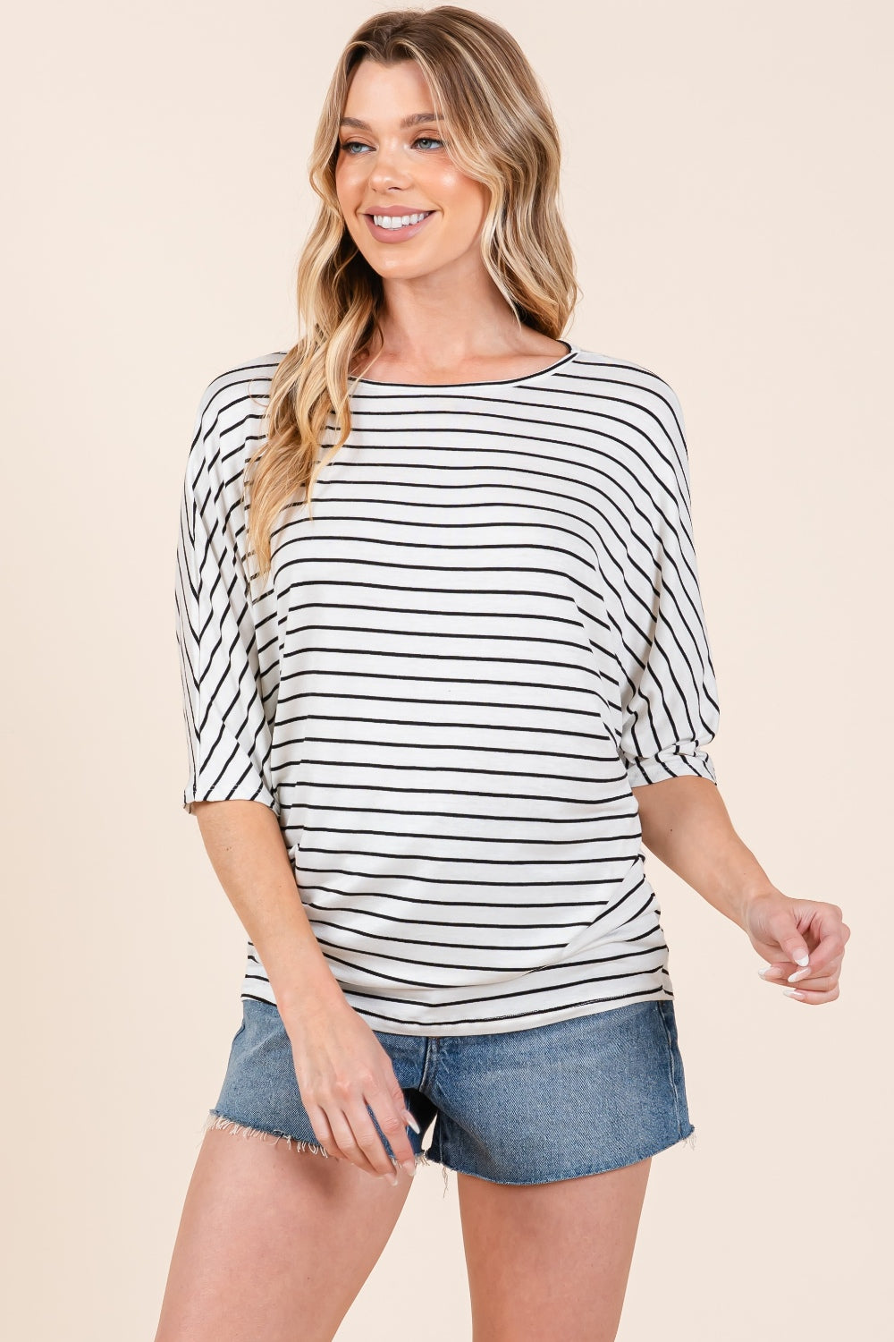 A person is wearing the BOMBOM Striped Boat Neck Dolman Sleeve Top paired with denim shorts, effortlessly embodying a wardrobe staple. The person has their right hand touching their hair and is looking down, against a plain, light-colored background.