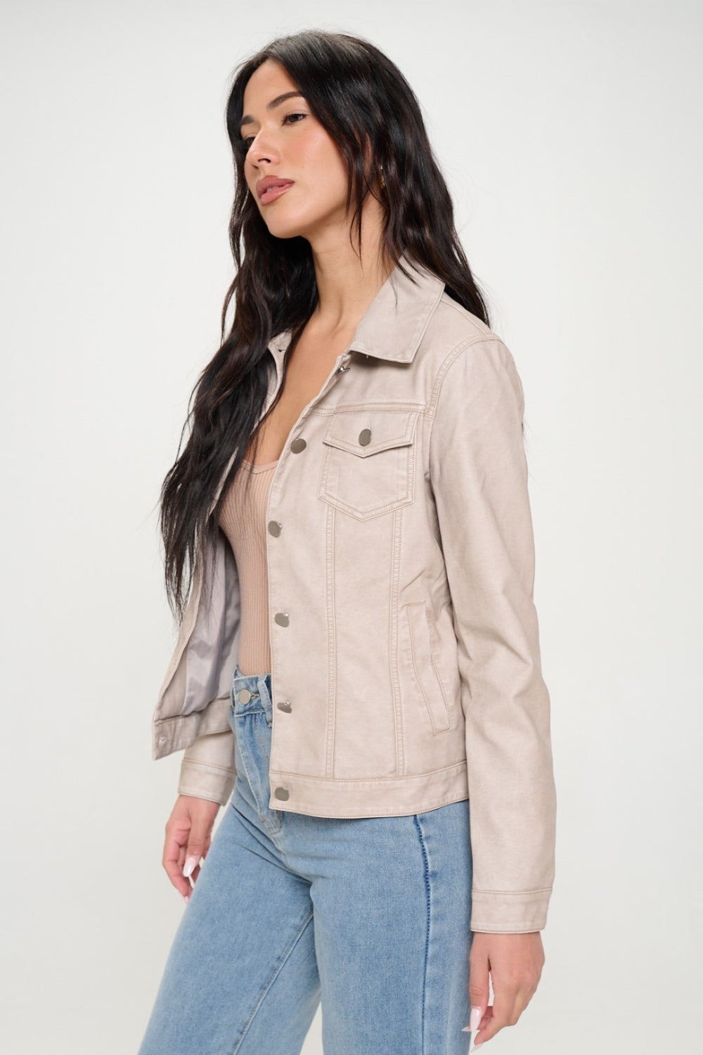 A woman with long dark hair, showcasing women's spring fashion, wears the Coalition LA Button Down Cargo Vegan Leather Shacket over a beige top and blue jeans as she stands against a plain background.