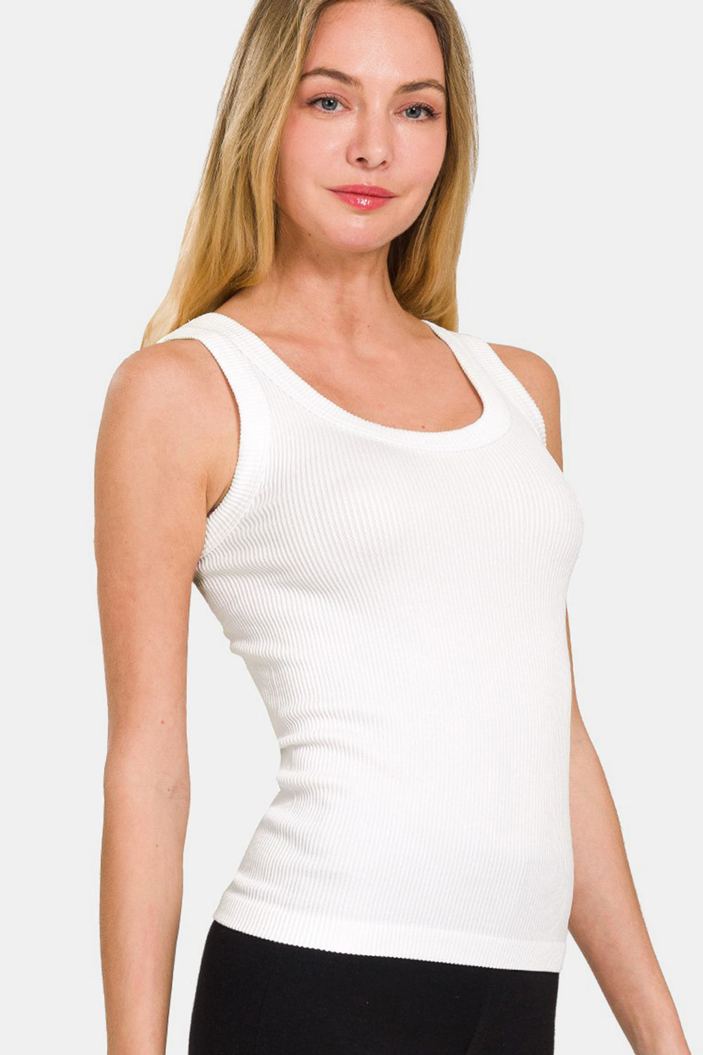 A woman with long blonde hair wears the Zenana 2 Way Neckline Washed Ribbed Tank in white, paired with black pants. She stands against a plain white background, highlighting her versatile wardrobe choices.